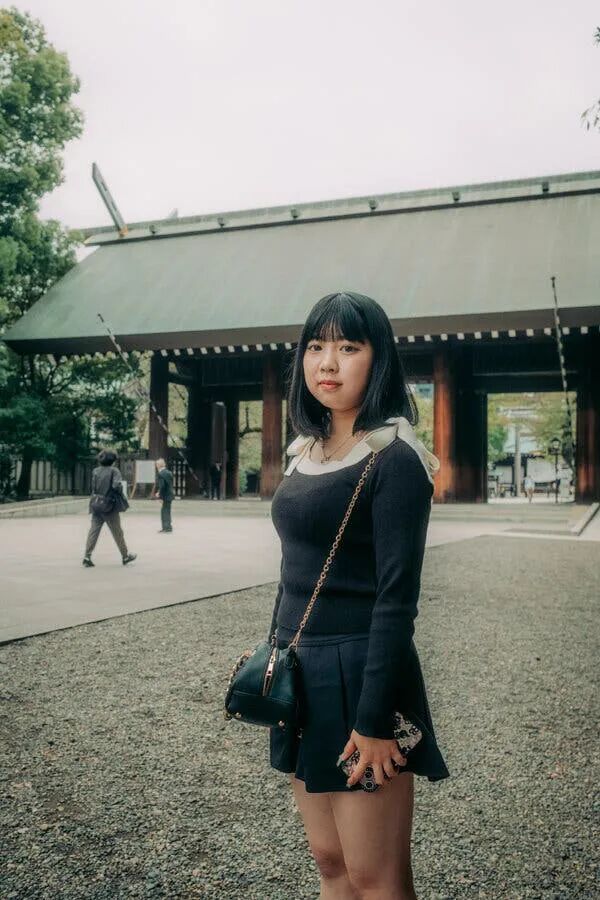 A young woman wearing black stands in front of a grand entrance with a slanted roof.