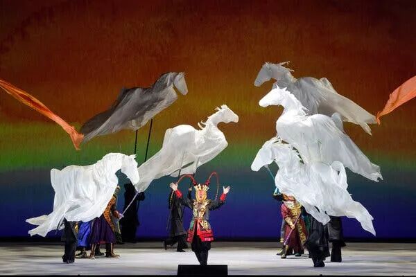 A man sings surrounded by horse puppets made of white billowy fabric.
