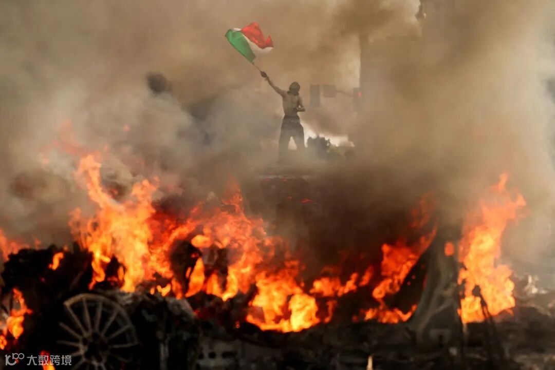 A man waves a Mexican flag as smoke and flames rise from a burning vehicle during a protest against federal immigration sweeps, near Los Angeles City Hall in downtown Los Angeles, California, on Sunday.