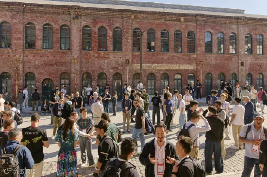 大批年轻人聚集在历史红砖建筑前的鹅卵石广场，大家衣着休闲、佩戴工牌，三五成群交流社交