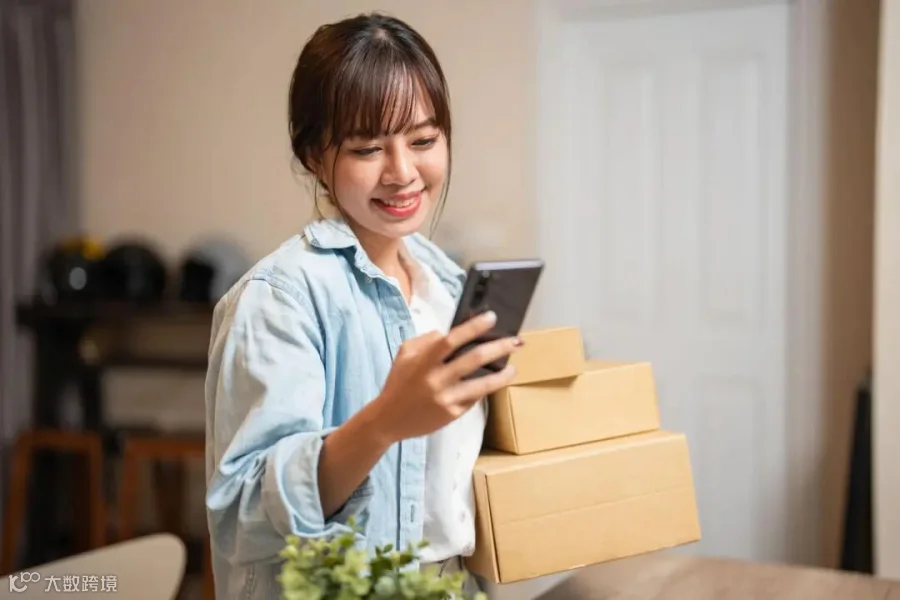 A young Asian woman is sitting at home, using her credit card and phone/laptop to make an online shopping transaction.